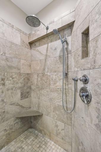 Updated tile shower in the primary bath with the convenience of a handheld shower head and a built-in bench.