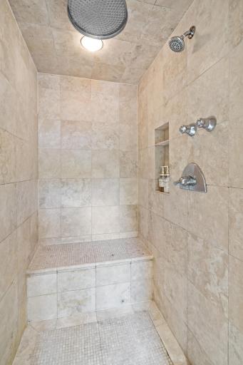 The primary bathroom custom steam shower features floor-to-ceiling luxe tile, a rain showerhead, a built-in niche, and a glass enclosure - a shower worth lingering in.