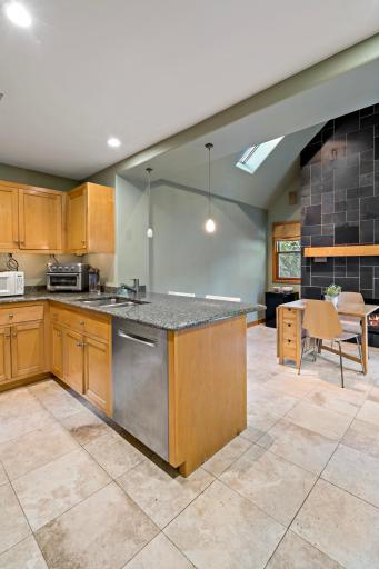Open-concept kitchen and dining with vaulted ceilings, skylights, granite counters, and a dramatic slate fireplace sourced from the historic Ramsey County Courthouse.