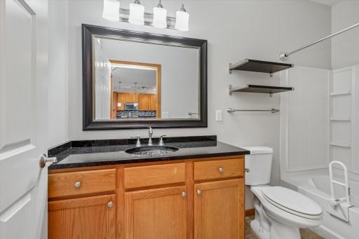 Bright, clean bathroom featuring a spacious vanity, granite countertop, oak cabinetry and tub/shower combination with convenient built-in storage