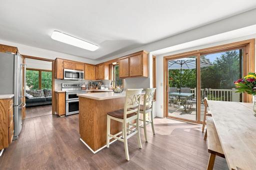 Bright, open-concept kitchen and dining area featuring stainless steel appliances, central peninsula seating, and sliding glass door with access to the back deck.