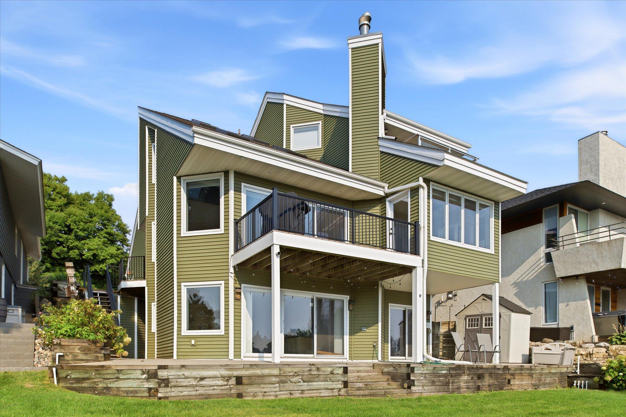 Prior Lake lakefront living! Lakeside exterior showcasing the newly installed deck railing system, multiple outdoor living spaces and direct access to the shoreline and private dock.
