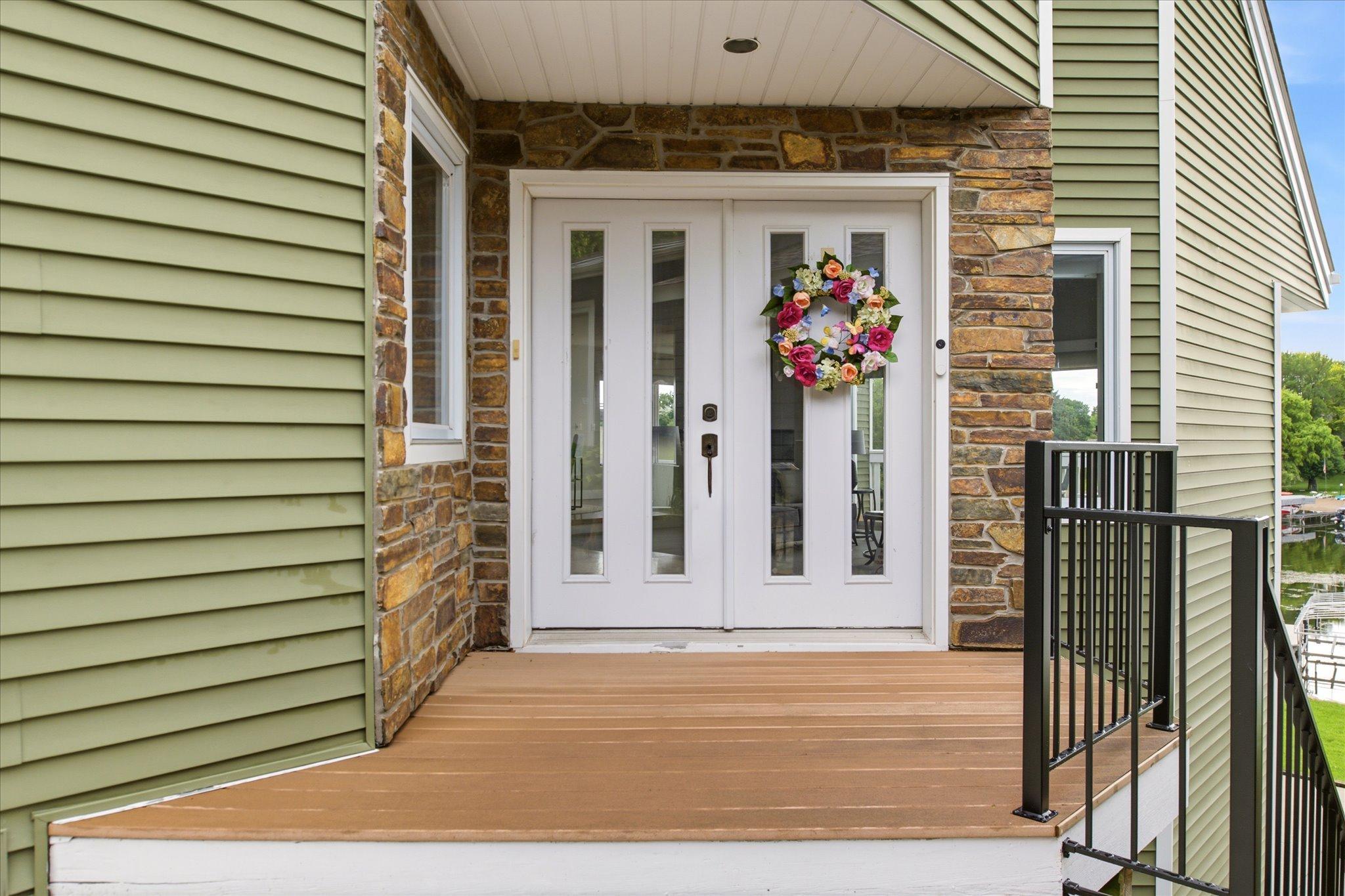 Covered front entry featuring double doors, natural stone accents, composite decking, and newly installed black iron railings.