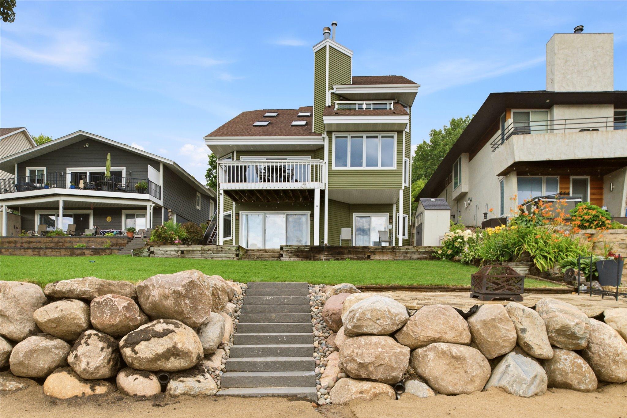 Rear elevation featuring the newly installed boulder shoreline retaining wall with steps providing access to the beach and lake.