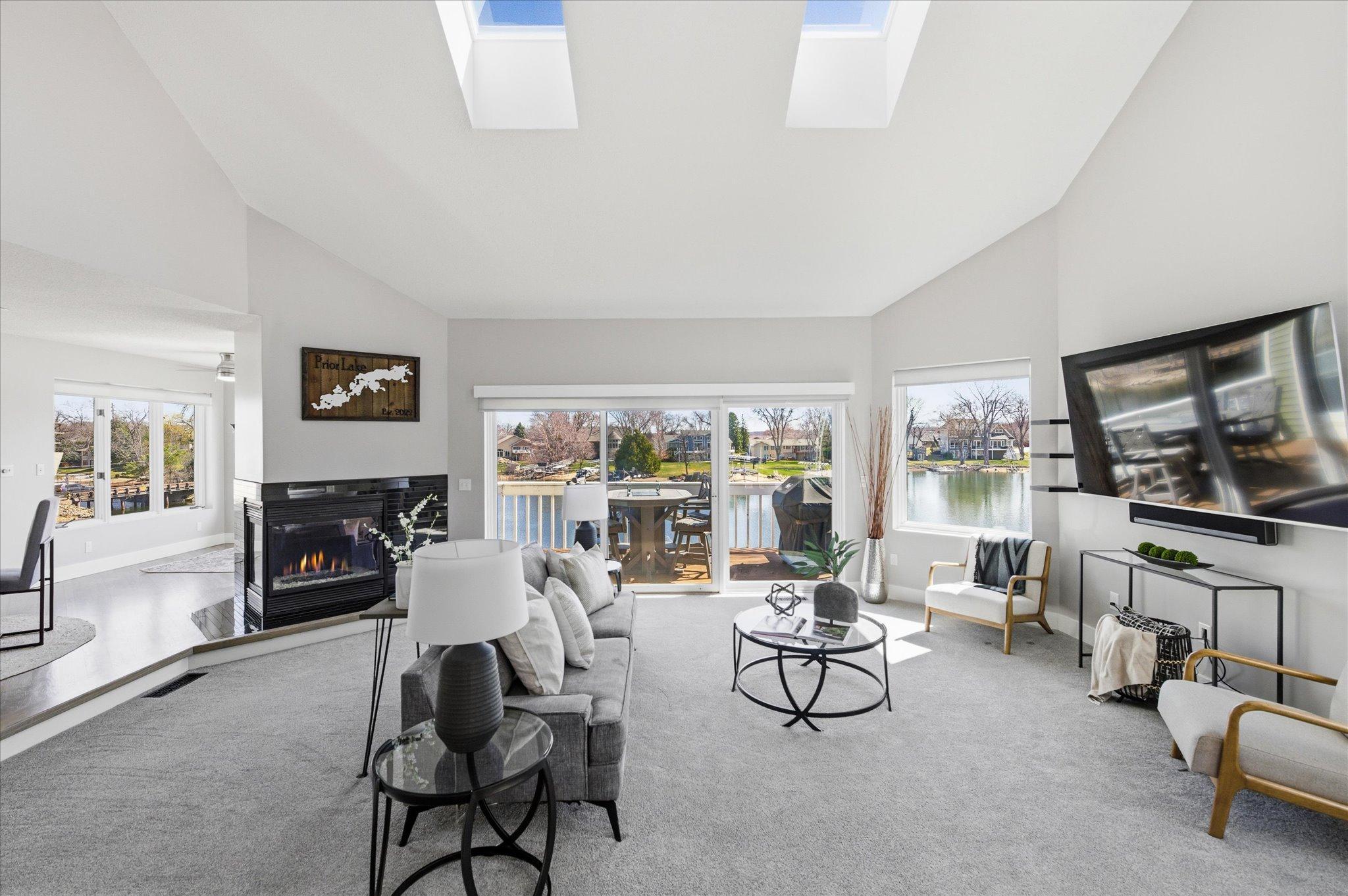 Living room with vaulted ceilings, gas fireplace, expansive windows, and sliding doors to the lakeside deck.