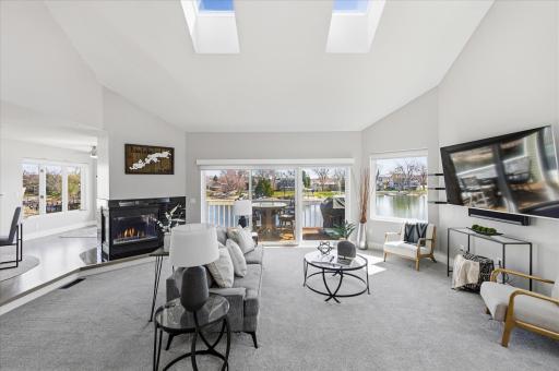 Living room with vaulted ceilings, gas fireplace, expansive windows, and sliding doors to the lakeside deck.