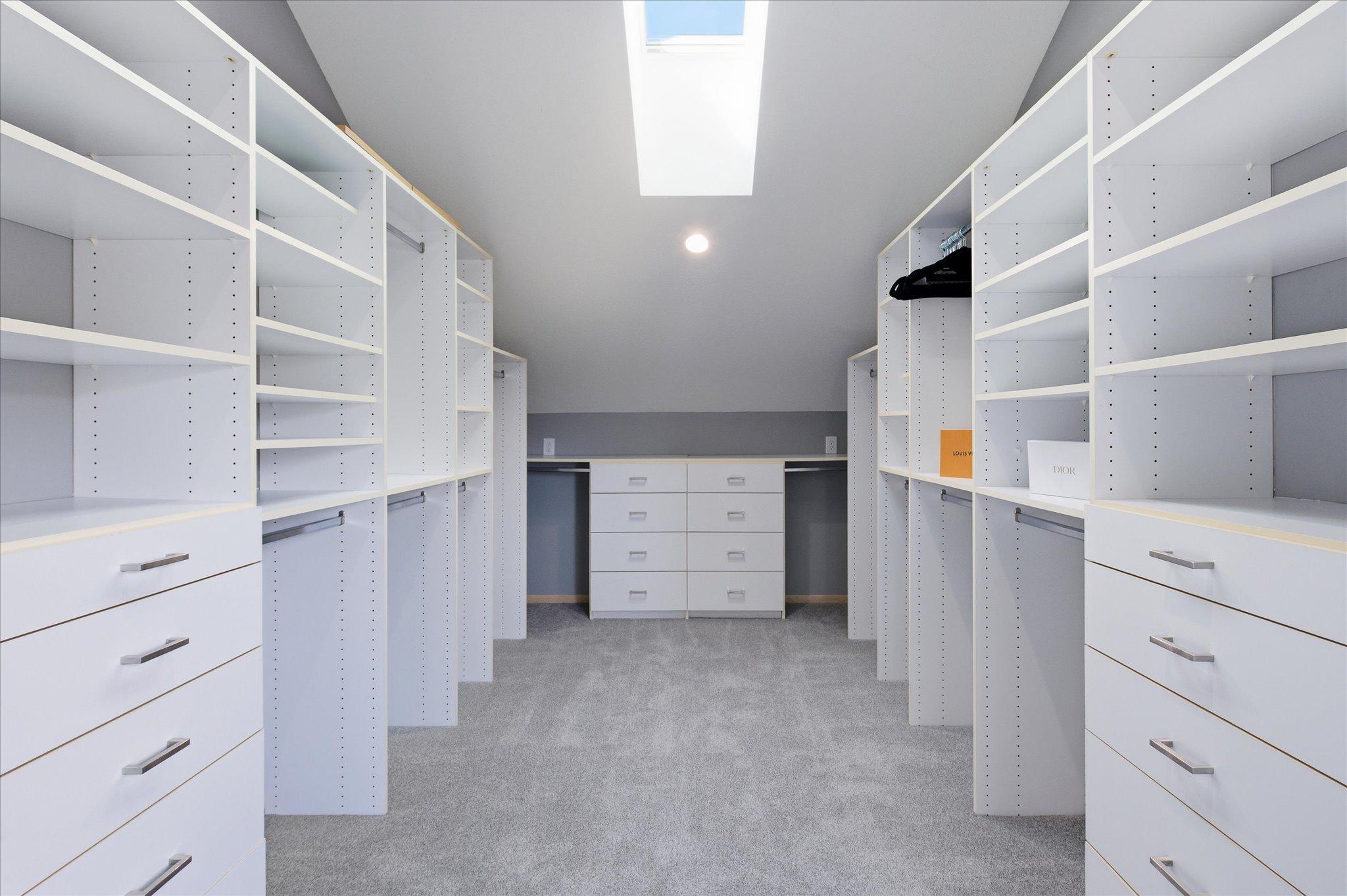 Walk-in closet with custom organization system, built-in drawers, and skylight.