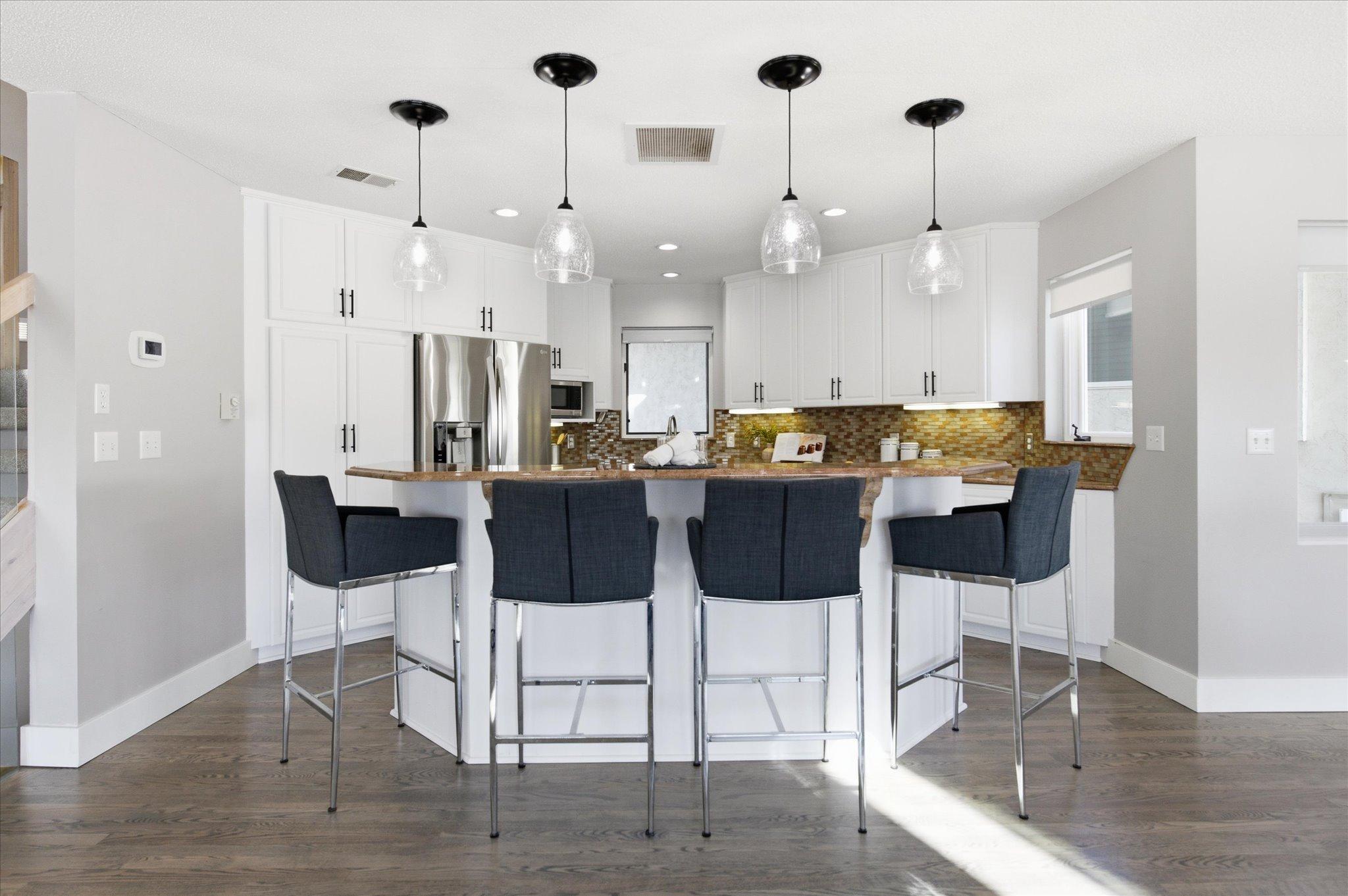 Kitchen with center island, breakfast seating, white cabinetry, granite countertops, and stainless steel appliances.