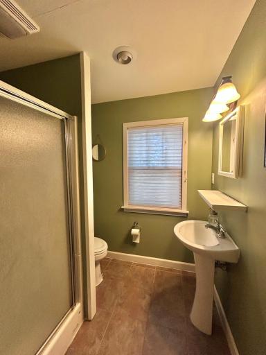 This bathroom is located off the front entry next to the second bedroom. Heated tile flooring, shower, toilet, storage cabinet above toilet, pedestal sink with a medicine cabinet on the wall.