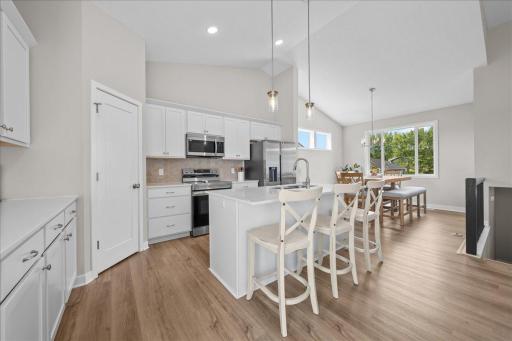 Bright, open kitchen featuring abundant cabinetry, quartz countertops, stainless steel appliances, a large center island with seating, and a convenient pantry.