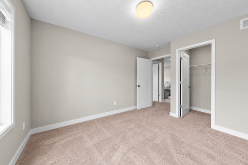Bright bedroom with neutral carpeting, large closet and natural light.