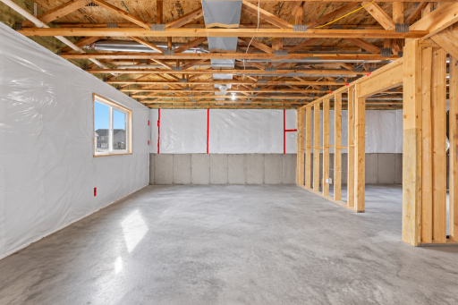 Unfinished lower-level space with window, concrete floor and framing already in place.