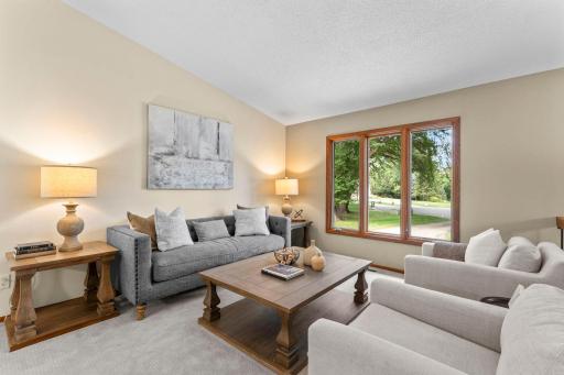The main level features a spacious living room with vaulted ceilings, carpeting, and large front-facing windows that fill the space with natural light.