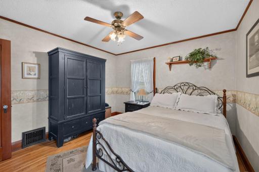 Primary main-floor bedroom features hardwood floors, natural wood trim and windows on two sides.