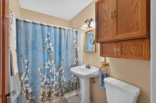 The full bathroom features a pedestal sink, tub/shower combination and wood storage cabinetry.