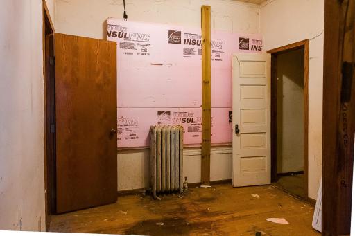 Main level bedroom, windows damaged and covered over. Door to the right is a walk-in closet (under stair well), door to the left is the main level full bath