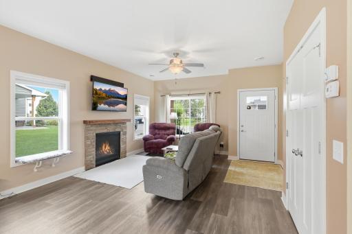 Bright and Inviting Main-Level Living Room Featuring a Cozy Gas Fireplace with Stone Surround, Luxury Vinyl Plank Flooring, and Multiple Windows Providing Plenty of Natural Light