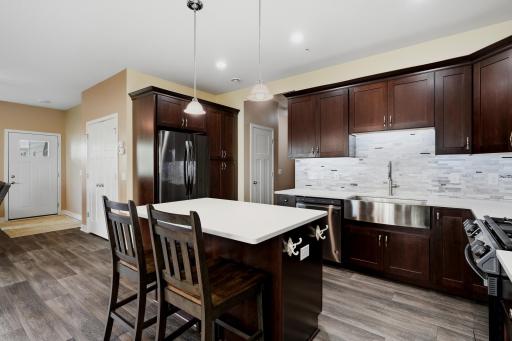 Beautifully Appointed Kitchen Featuring New Matte-Finish Quartz Countertops (2025), a New Kitchen Faucet, Rich Toned Cabinetry, Stainless Steel Appliances, a Large Center Island with Seating. A Large Farm Sink and Lower Cabinet Rollouts