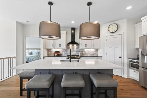 This massive center island is the heart of the kitchen with Quartz countertops, an island sink, generous storage underneath, pull-out trash and recycling, and stunning custom light fixtures that tie it all together perfectly.