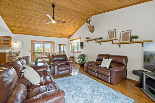 Cozy open-concept living room featuring vaulted wood ceilings, rich leather seating, warm natural light, and rustic cabin-inspired details.