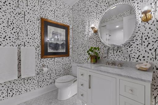 Visual Comfort lighting and Schumacher wallcovering give the guest bath a distinctive designer finish. Carrara marble flooring continues the elevated material palette into the guest bath.