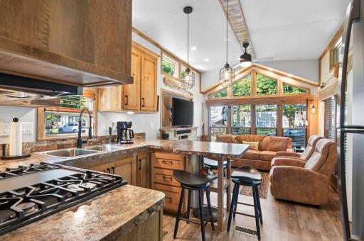 This open-concept layout seamlessly connects the kitchen and main living space under vaulted ceilings framed by expansive floor-to-ceiling gable windows.