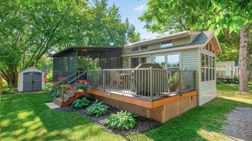 A spacious elevated wooden deck runs along the front of the home, featuring built-in lighting steps, a safety railing, and ample space for outdoor dining and grilling.