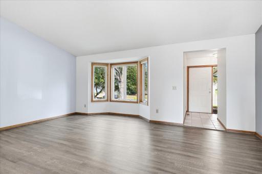 Bright and spacious living room featuring LVP flooring, vaulted ceilings, and a large bayed window that fills the space with natural light.