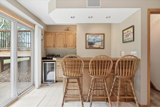 The lower-level wet bar is ready for entertaining, featuring a built-in refrigerator, tile flooring, ample cabinetry and counter space, plus recessed accent lighting that adds a warm ambiance to the space.