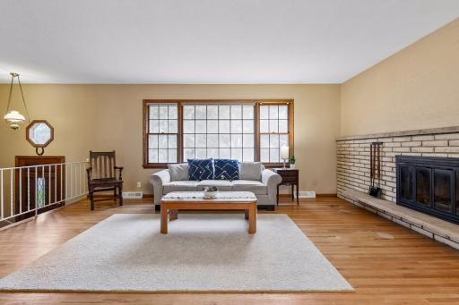 Spacious main-level living room with original red oak hardwood floors, a large picture window and beautiful brick fireplace.