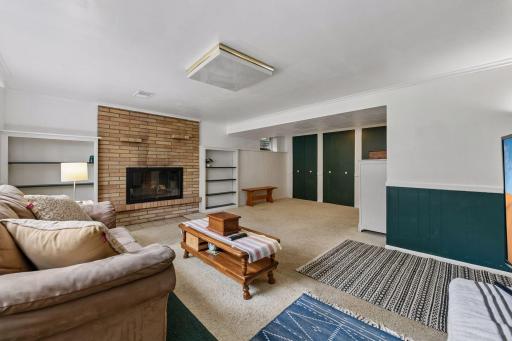Spacious lower-level family room with a second brick fireplace, built-in shelving and plenty of flexible living space.
