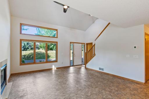 Light-filled living room with vaulted ceiling, large windows, fireplace and open staircase. The whole home was just painted in Sherwin William Shoji White color.