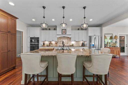 The kitchen is a chef’s dream, offering abundant soft-close cabinetry, stainless steel appliances, granite countertops, and a large center island with breakfast bar seating and pendant lighting.