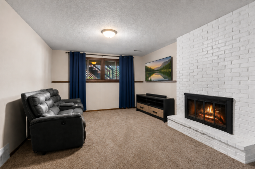 Cozy lower-level family room featuring plush carpet and a beautiful brick fireplace!
