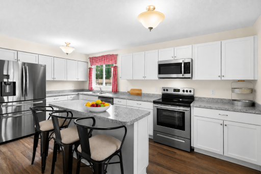 Bright & stylish kitchen featuring white cabinetry, stainless steel appliances, gorgeous countertops and a large center island with seating!