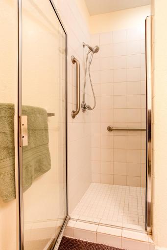 Large tiled walk-in shower features a built-in bench, glass door, handheld showerhead, and grab bars.