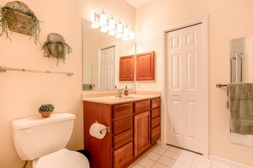 Spacious primary bath includes a large vanity, oversized mirror, tile flooring, and convenient adjoining closet.