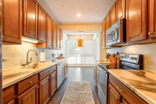 Gourmet galley-style kitchen features abundant cabinetry, generous counter space, stainless-steel appliances, and a light-filled dining nook with panoramic windows.
