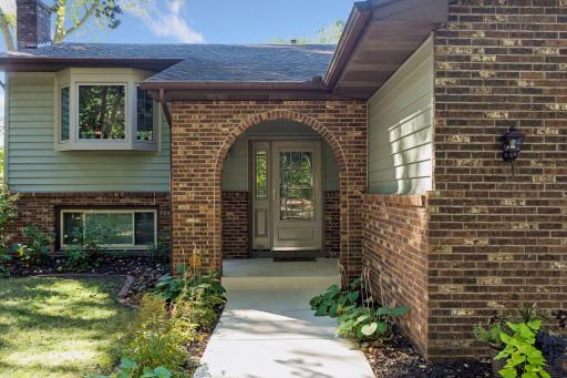 Welcoming front entrance featuring a charming brick archway, covered porch, and classic decorative front door with matching side glass panels!
