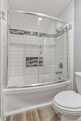 Another view of the main level bathroom showcasing the pristine white subway tile tub surround, custom mosaic accents, and sleek glass doors!