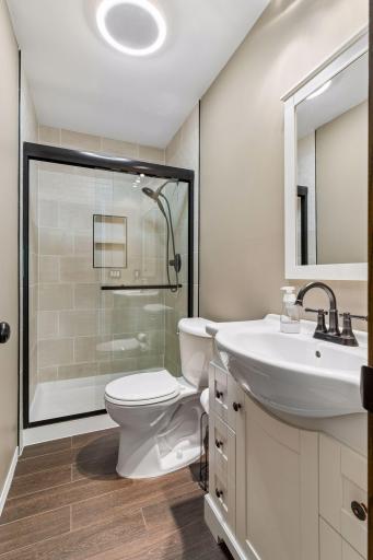 Fully remodeled private primary bath featuring a modern walk-in tile shower with glass doors, elegant vanity, and updated plank flooring!
