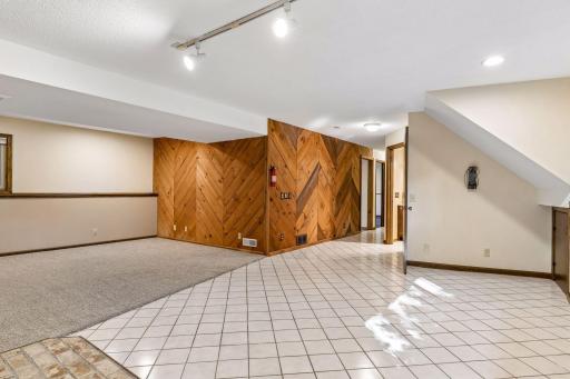 Another angle of the expansive lower level, showcasing the distinctive chevron wood paneling accents, crisp tile flooring, and clean neutral paint.