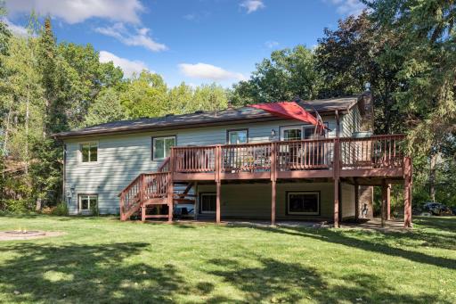 Spacious backyard oasis featuring an expansive raised deck, patio space, fire pit area, and a large, flat lawn surrounded by mature trees!