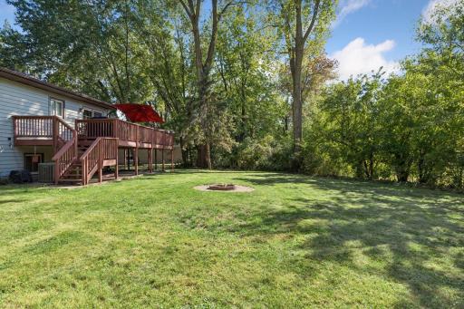 Another angle showcasing the expansive, flat backyard oasis complete with a central brick fire pit, lush green lawn, and towering mature trees!