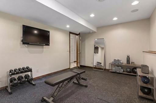 Flexible fifth bedroom on the lower level, currently staged as a home gym features durable gym flooring and built-in speakers. *Virtually staged to show design options.