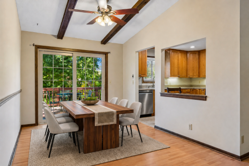 Sunlit dining area featuring high beamed ceilings, sliding doors to the deck, and a convenient pass-through cutout to the kitchen! *Virtually staged to show design options.