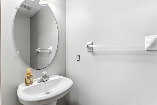 Guests get their own space in the main-level bathroom, with a pedestal sink and oval mirror in a crisp, neutral palette.
