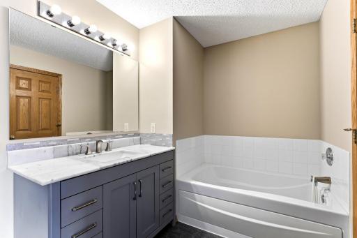 Soak in the tub in the primary ensuite, updated with a slate-blue vanity, marble-look counters, and a wide mirror under a five-light fixture.