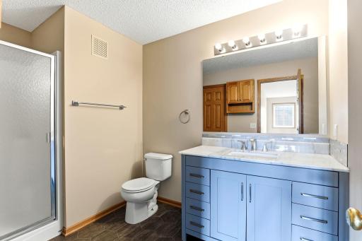 A blue shaker vanity with marble-look counters and a tiled backsplash freshens up the full bath, alongside a glass-door shower and hexagon tile floors.