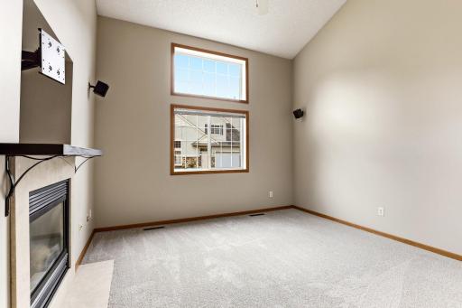Stacked windows climb toward the vaulted ceiling and fill the living room with daylight, while the gas fireplace and plush carpet make winter evenings feel cozy.